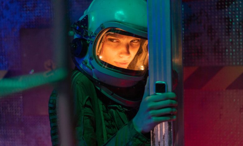 A woman astronaut in a helmet inside a sci-fi space vessel, surrounded by colorful lighting.