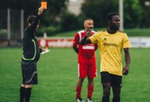 Referee issuing a red card to a soccer player in an outdoor match setting.