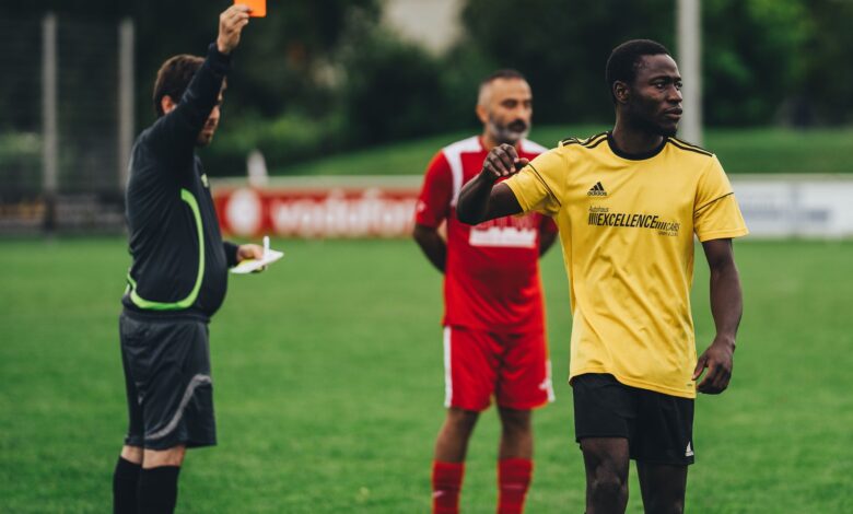 Referee issuing a red card to a soccer player in an outdoor match setting.