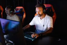 Two young men engaged in an intense esports gaming session with headsets in a dark room.