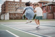 Two young girls jumping and playing together on a city playground.