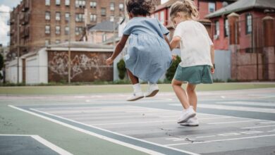 Two young girls jumping and playing together on a city playground.