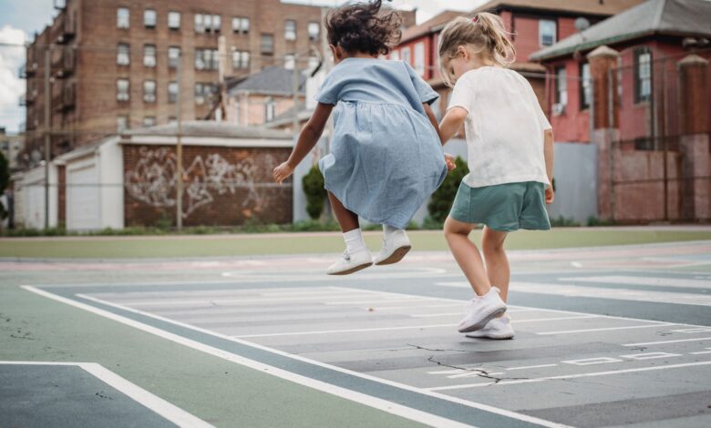 Two young girls jumping and playing together on a city playground.