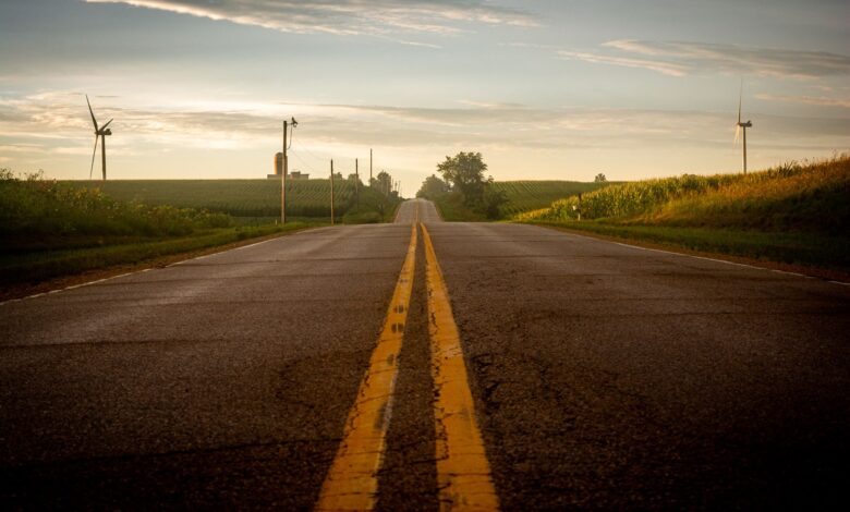 A scenic rural road flanked by wind turbines and fields under a summer sky.