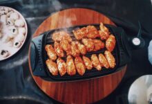 Top view of delicious spicy chicken wings grilling on an electric grill with mushrooms nearby.