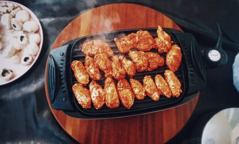 Top view of delicious spicy chicken wings grilling on an electric grill with mushrooms nearby.