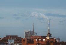 Factory with smokestack emitting smoke under a clear sky, industrial setting.