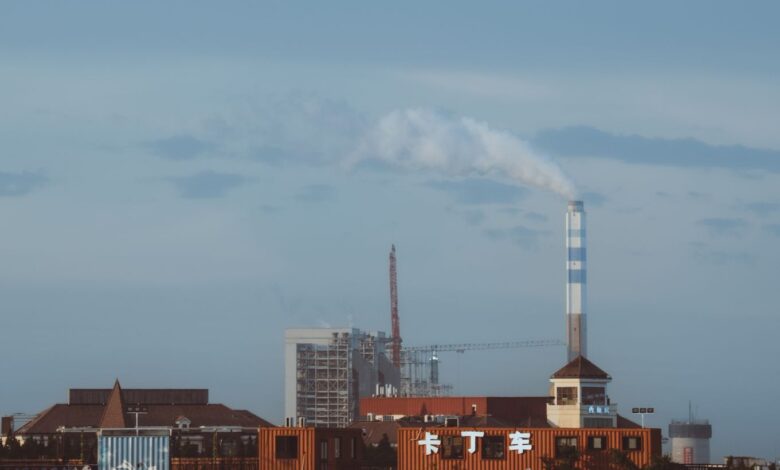 Factory with smokestack emitting smoke under a clear sky, industrial setting.