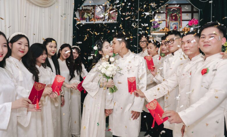 Bride and groom kiss amid festive wedding celebration with traditional attire and confetti.