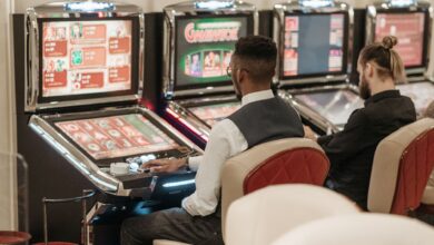 Two men engaged in gaming at a casino, seated at slot machines indoors.