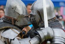Two medieval knights in full armor engaged in close combat during a reenactment.