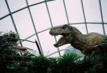 Animatronic T-Rex display in Singapore dome with caution sign amidst lush greenery.