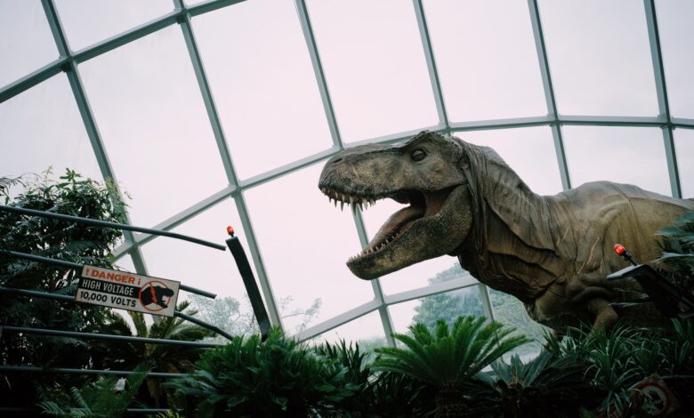 Animatronic T-Rex display in Singapore dome with caution sign amidst lush greenery.