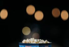 A close-up view of popcorn in a themed bucket with movie bokeh background.