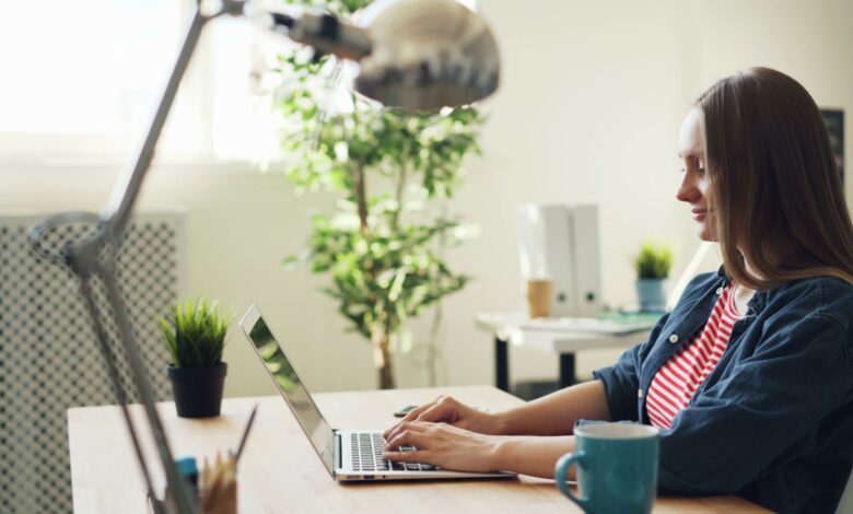 Woman smiling while working on a laptop in a modern office with plants.