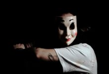 A mysterious figure wearing a mask creates a chilling atmosphere on a dark background.