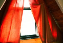 A cozy attic window with red curtains letting in warm sunlight, creating a serene indoor atmosphere.