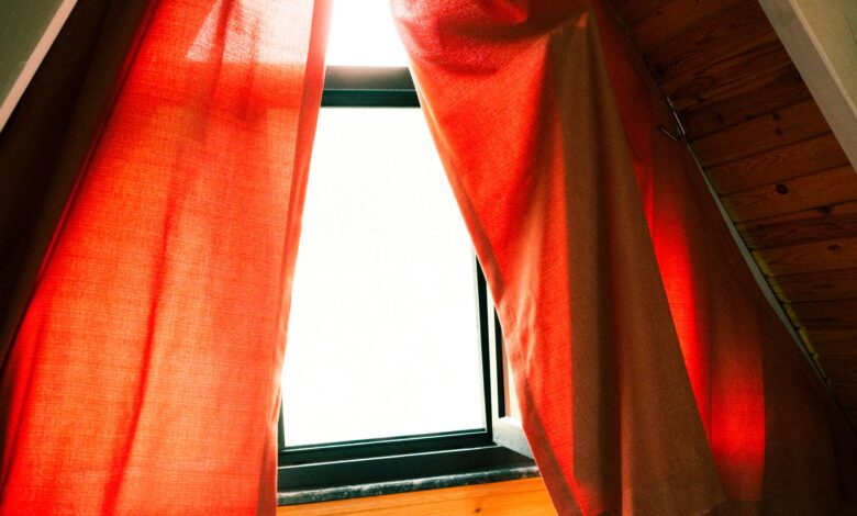 A cozy attic window with red curtains letting in warm sunlight, creating a serene indoor atmosphere.