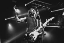 Black and white photo capturing an energetic guitarist performing live on stage.