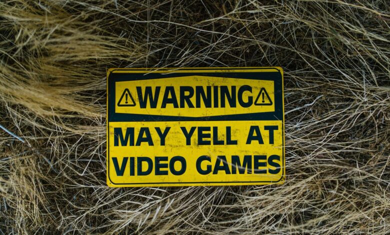 A funny yellow warning sign on grass reading 'Warning May Yell at Video Games'.