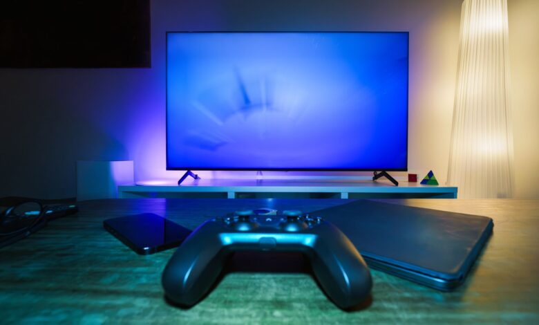 A stylish and ambient gaming setup featuring a controller, smart devices, and a TV in a lit living room.