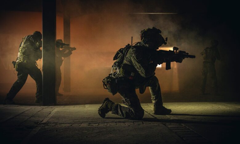 Four soldiers in tactical gear engage in a smoky nighttime military operation indoors.