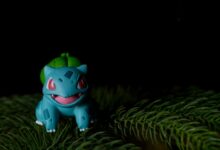 Vibrant Bulbasaur toy placed on pine needles with a dark background.