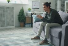 Smiling young man enjoying video games on a sofa at home.