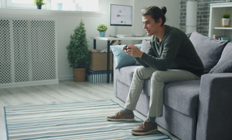 Smiling young man enjoying video games on a sofa at home.