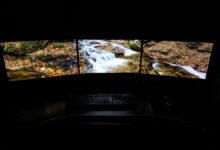 Modern computer with picturesque brook shown on screens placed on desk near keyboard and mouse in dark room