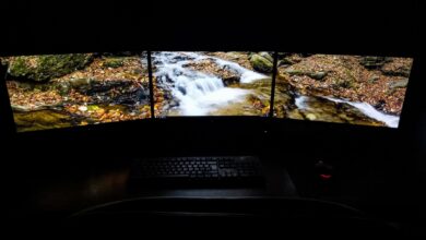 Modern computer with picturesque brook shown on screens placed on desk near keyboard and mouse in dark room