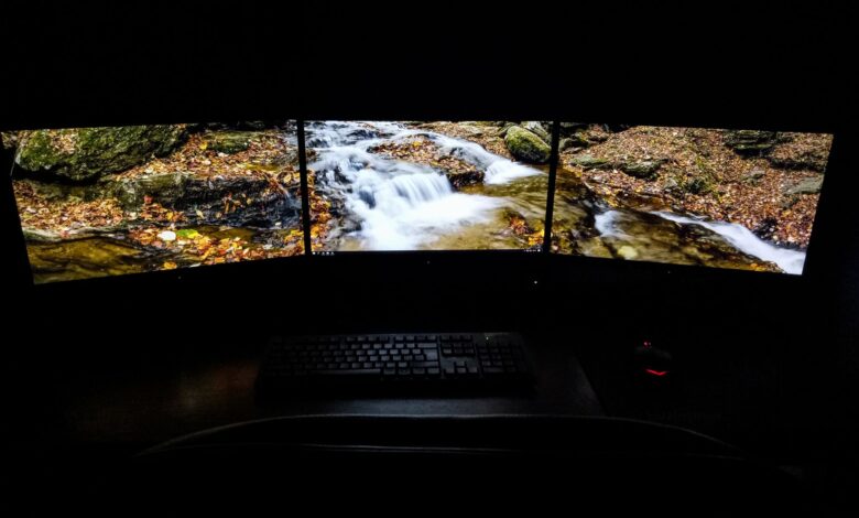 Modern computer with picturesque brook shown on screens placed on desk near keyboard and mouse in dark room