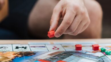 Crop unrecognizable man with artificial red house playing board game at table on weekend