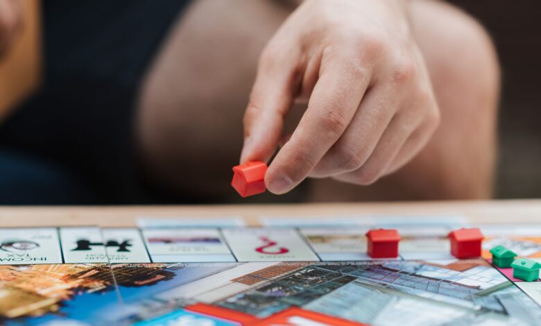 Crop unrecognizable man with artificial red house playing board game at table on weekend