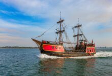 A vibrant pirate ship sails on a clear day, showcasing its vintage wooden structure and colorful design.