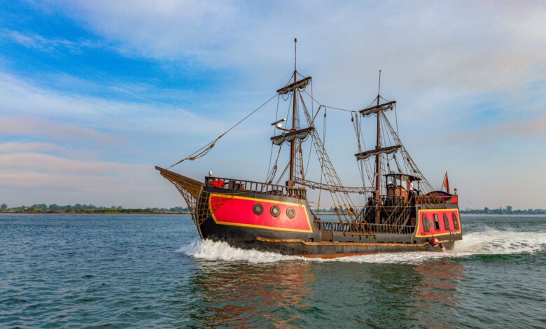 A vibrant pirate ship sails on a clear day, showcasing its vintage wooden structure and colorful design.