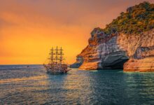 A majestic sailing ship navigates past stunning sea cliffs at sunset, offering a picturesque view of adventure.