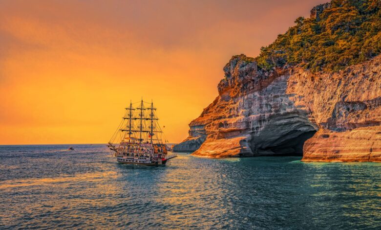 A majestic sailing ship navigates past stunning sea cliffs at sunset, offering a picturesque view of adventure.