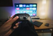Close-up of a person holding a gaming controller in a cozy living room setup with TV.