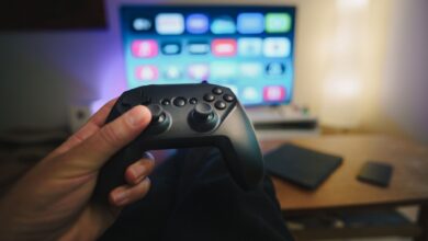 Close-up of a person holding a gaming controller in a cozy living room setup with TV.