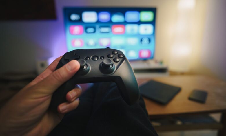 Close-up of a person holding a gaming controller in a cozy living room setup with TV.