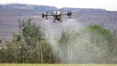 High-tech drone spraying crops in a field with mountains in the background, showcasing modern farming technology.