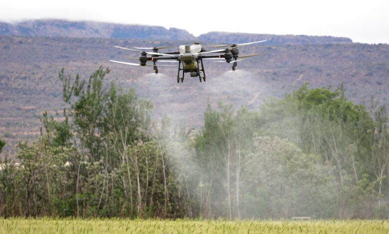 High-tech drone spraying crops in a field with mountains in the background, showcasing modern farming technology.