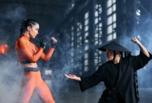 Two cosplayers engage in a dynamic martial arts duel amidst dramatic fog, indoors.