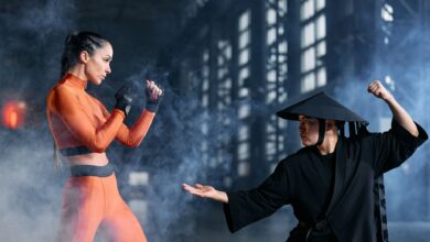 Two cosplayers engage in a dynamic martial arts duel amidst dramatic fog, indoors.
