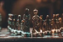 Close-up of gold chess pieces on a chessboard in a dimly lit room.