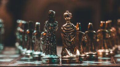 Close-up of gold chess pieces on a chessboard in a dimly lit room.