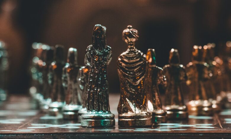Close-up of gold chess pieces on a chessboard in a dimly lit room.