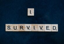 Wooden Scrabble tiles spelling 'I Survived' on a dark surface conveying strength and resilience.