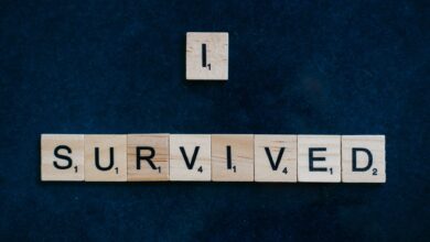 Wooden Scrabble tiles spelling 'I Survived' on a dark surface conveying strength and resilience.